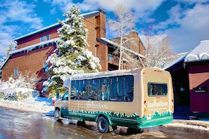 A Steamboat Resorts bus parked in front of a building with a snow-covered tree.