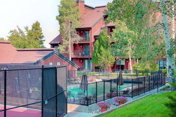 A residential building with a swimming pool, outdoor seating, and a fenced patio area.