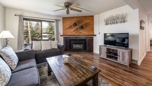 Una sala de estar con sofá, mesa de centro, chimenea, televisión y ventilador de techo.