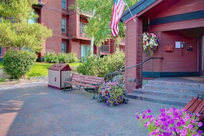 A red building with a flag, steps, a bench, and a flower bed.