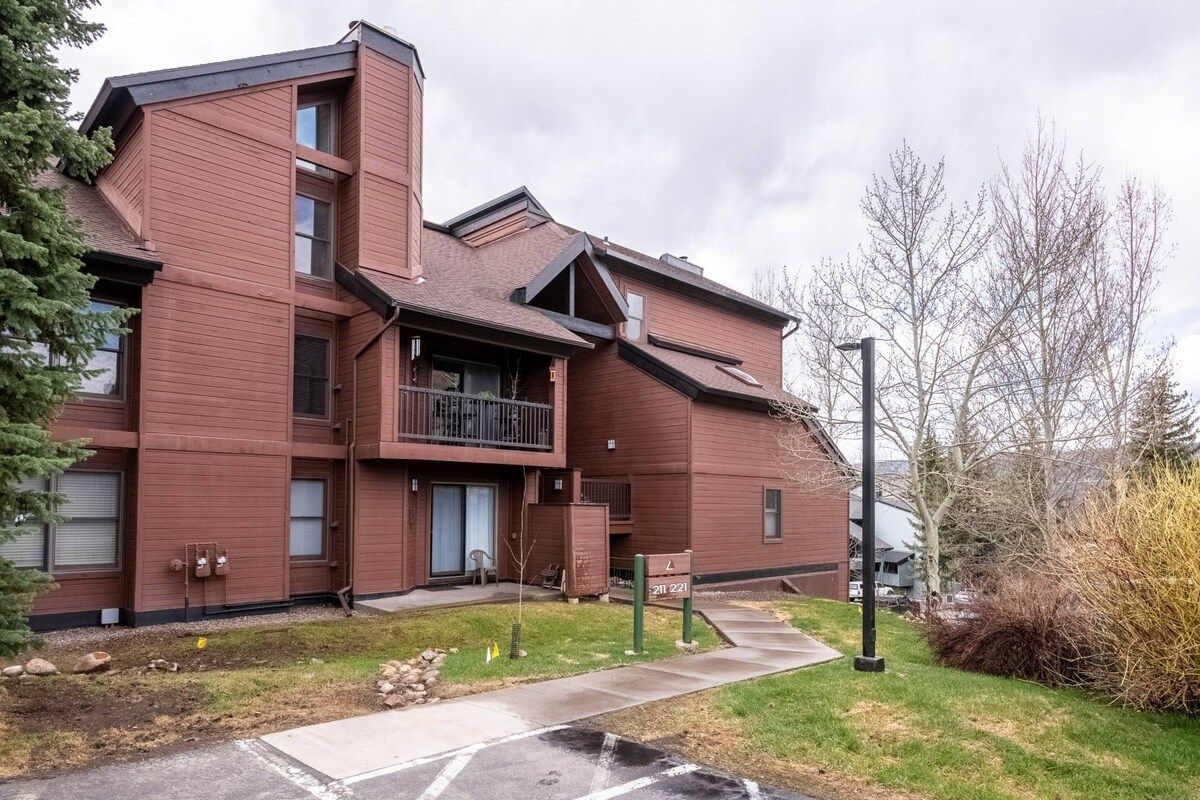 A multi-story residential building with a balcony, a small front yard, and a visible address sign.