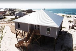 Ein Strandhaus mit Metalldach, einer Holzterrasse und einer Treppe zum Eingang.