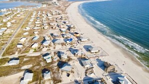 An aerial view of a coastal area with numerous small, clustered buildings along the beach, suggesting a vacation or resort setting. - Steps from the Beach! Water view from each bedroom! Great for multiple families! (Dauphin Island)