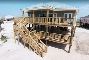 Una casa de playa de madera de dos pisos con balcón, una escalera y techo de metal.