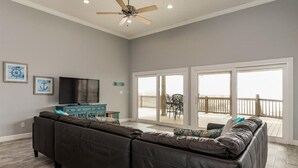 A spacious living room with a large sectional sofa, a flat-screen TV, and a ceiling fan. - Steps from the Beach! Water view from each bedroom! Great for multiple families! (Dauphin Island)