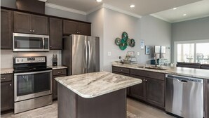 A modern kitchen with dark wood cabinets, stainless steel appliances, a marble island, and a view of the city through large windows. - Steps from the Beach! Water view from each bedroom! Great for multiple families! (Dauphin Island)