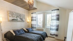 A bedroom with two beds, a wooden floor, a window with curtains, and a painting on the wall.