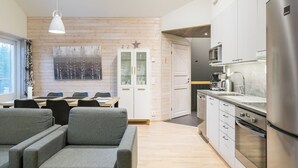 A modern kitchen with stainless steel appliances, a dining area with a wooden table and grey chairs, and a white cabinet with glass doors.
