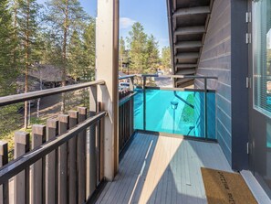 A balcony with a view of a swimming pool, wooden deck, and a metal railing.