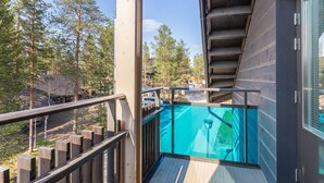 A balcony with a wooden floor, a metal railing, and a view of a road and trees.