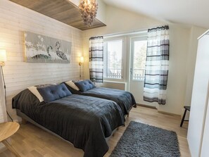 A room with two beds, a wooden floor, a painting on the wall, and a window with curtains.