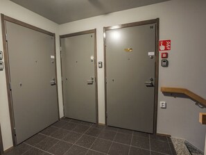 Een gang met drie deuren, genummerd 7, 8 en 10, en een rookmelder aan de muur.