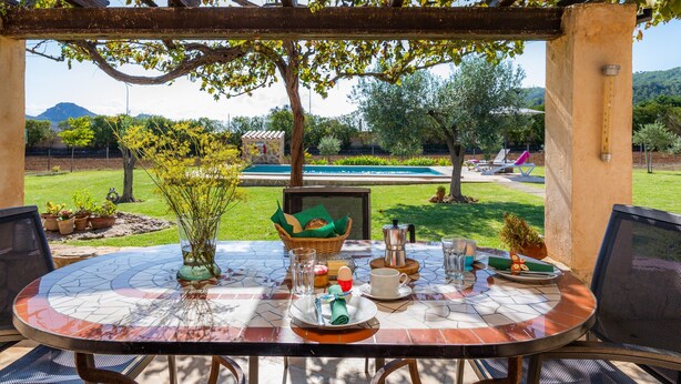 Eine Terrasse im Freien mit einem runden Esstisch, umgeben von Stühlen, mit Blick auf Pool und Garten.