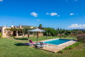 A swimming pool with lounge chairs and an umbrella, surrounded by a well-maintained lawn and a stone building.
