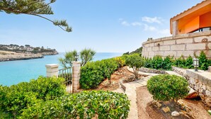 A coastal property with a view of the sea, a stone wall, and a well-maintained garden. - Villa Es Mirador with Sea View, Wi-Fi, A/C, Terrace & Garden; Parking Available (Cala Anguila-Cala Mendia)