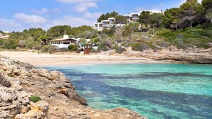 A coastal hotel with a beach view, rocky shoreline, and buildings on a hillside. - Villa Es Mirador with Sea View, Wi-Fi, A/C, Terrace & Garden; Parking Available (Cala Anguila-Cala Mendia)