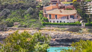 A coastal house with a stone facade, a balcony, and a view of the sea. - Villa Es Mirador with Sea View, Wi-Fi, A/C, Terrace & Garden; Parking Available (Cala Anguila-Cala Mendia)