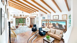 A spacious living area with wooden beams, a sofa, chairs, a coffee table, and a view of the sea. - Villa Es Mirador with Sea View, Wi-Fi, A/C, Terrace & Garden; Parking Available (Cala Anguila-Cala Mendia)