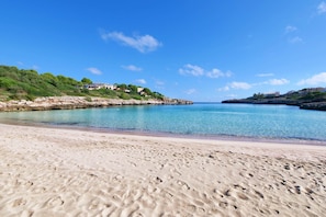 Une plage parsemée d’empreintes, un ciel dégagé et des bâtiments situés sur le flanc d’une colline.