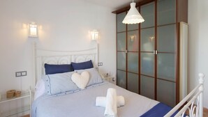 Ein ordentlich bezogenes Bett mit einem herzförmigen Kissen, einem weißen Kopfteil und einem Glasvitrine mit satinierten Glastüren.