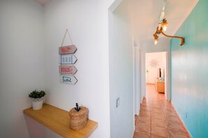 A hallway with a wooden shelf, a wall-mounted sign with motivational phrases, and a hanging light fixture.