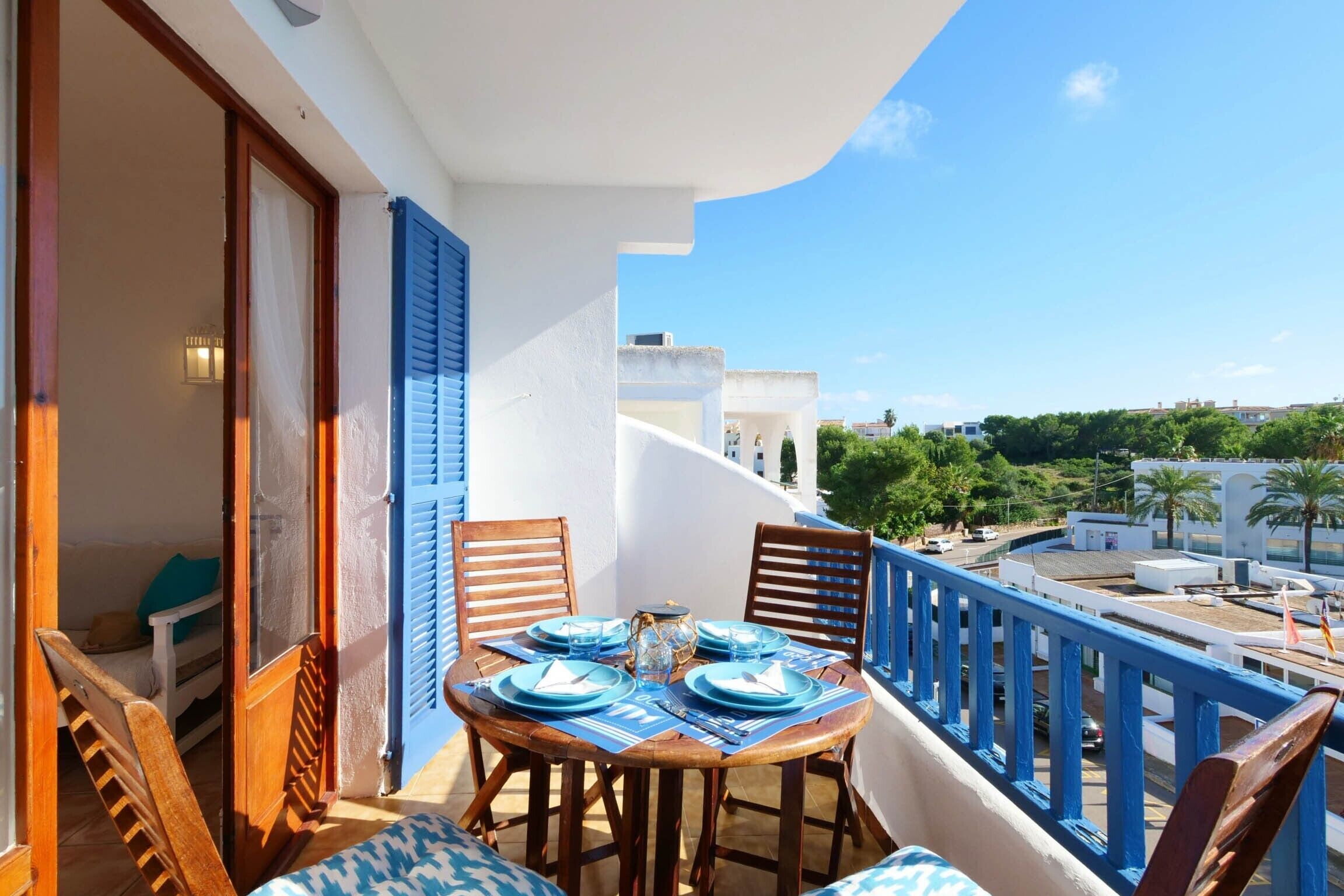 A balcony with a table set for dining, wooden chairs, and a view of the city.