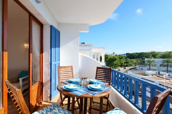 A balcony with a table set for dining, wooden chairs, and a view of the city.