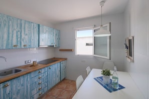 Une cuisine avec des meubles bleus, un plan de travail blanc, un évier et une table à manger avec des chaises.