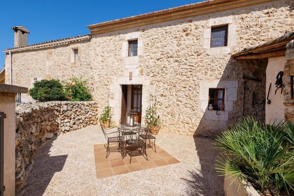 A stone building with a courtyard, a table with chairs, and a potted plant.