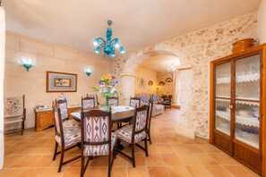A dining area with a round table, chairs, a chandelier, and a stone wall.