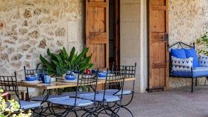 Un muro de piedra, puertas de madera, una mesa con sillas y un sofá azul con estampado.