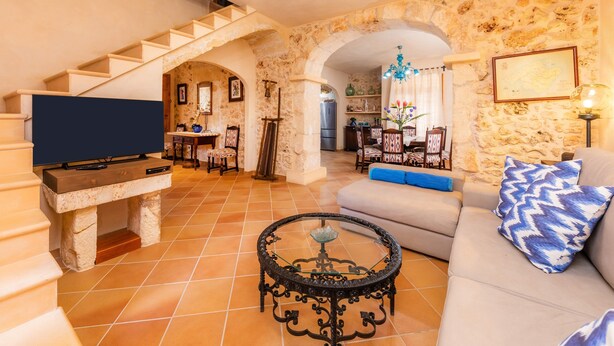 Una sala de estar con pared de piedra, una escalera, un sofá, una mesa de centro y una televisión.
