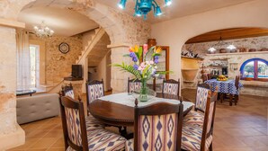 Un comedor con una mesa redonda, sillas estampadas, un jarrón con flores y paredes de piedra.