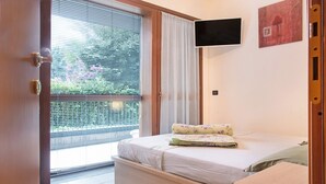 Une chambre à coucher avec un lit, un téléviseur fixé au mur et une porte-fenêtre coulissante donnant sur un balcon.