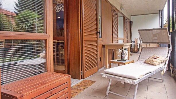 Une pièce comprenant un lit, un banc en bois, une petite table et une fenêtre avec des stores.
