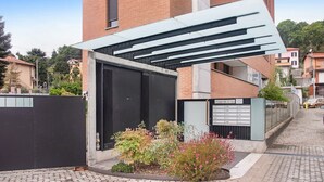 Un bâtiment moderne doté d’une entrée abritée, d’une allée bordée de portails et d’un petit jardin agrémenté de plantes à fleurs.