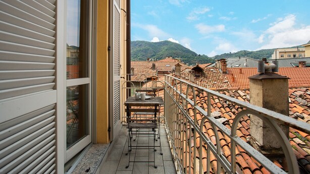 A balcony with a table and chairs, overlooking a cityscape with terracotta rooftops and a mountain in the distance. - Delightful Holiday Apartment Steps from the Port with Mountain Views (como)