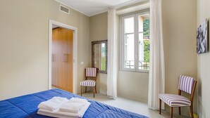 A bedroom with a bed, a chair, a wardrobe, a window with curtains, and a mirror. - Delightful Holiday Apartment Steps from the Port with Mountain Views (como)