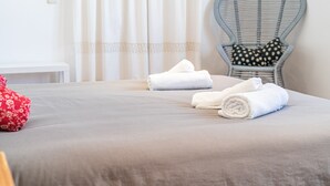 A neatly made bed with two rolled towels, a red floral pillow, and a wicker chair with a polka-dotted cushion. - Holiday Home "Ana House" with Sea View, Wi-Fi & Terrace (CAN PASTILLA)