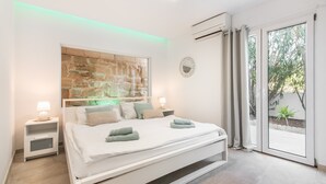 Une chambre moderne avec un lit, des tables de chevet, un miroir fixé au mur et une porte-fenêtre coulissante donnant sur un balcon.