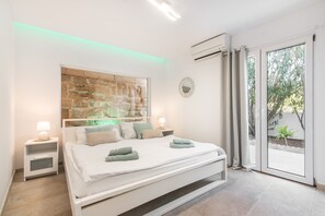A modern bedroom with a bed, nightstands, a wall-mounted mirror, and a sliding glass door leading to a balcony.
