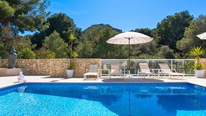 Une piscine d’un bleu éclatant, bordée de chaises longues et d’ombrelles, et entourée de murs de pierre et d’arbres.