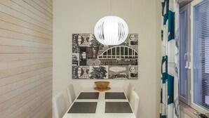 A dining area with a white table and chairs, a wall-mounted light fixture, and a cityscape artwork.