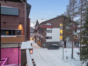 A snow-covered street with buildings, a car parked on the side, and a pedestrian walking in the distance.