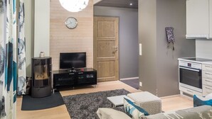 A modern living room with a flat-screen TV, a fireplace, a sofa, and a kitchen area with a stove.