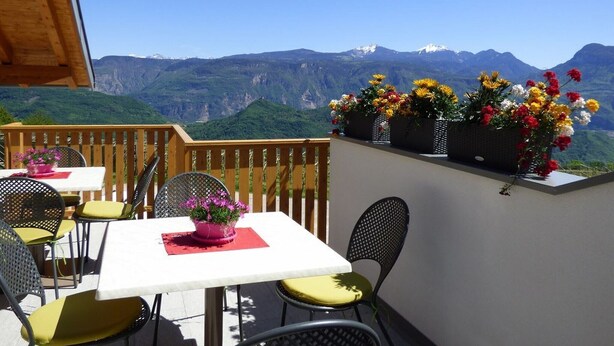 A balcony with a table and chairs, a wooden railing, and a view of mountains.