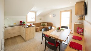 A compact kitchen with a dining area, a sofa, and a TV mounted on the wall.
