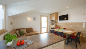 A modern kitchen with a dining area, a sofa, and a TV mounted on the wall.