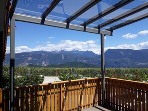Un balcón con vistas a montañas, barandilla de madera y cerramiento de vidrio.