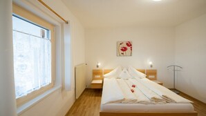 A bedroom with a wooden bed, a radiator, a window with lace curtains, and a wall-mounted artwork.